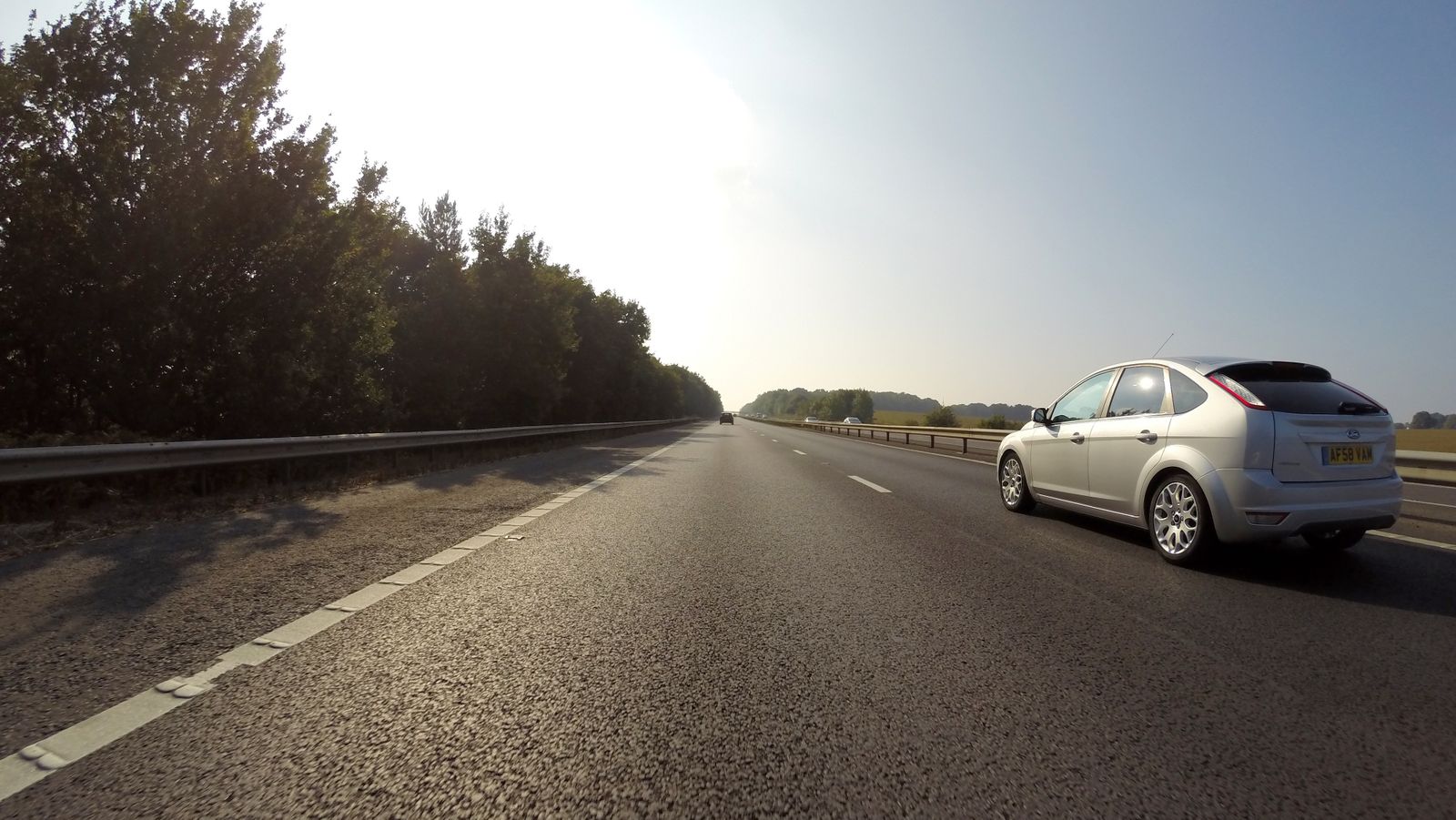 Car on a UK dual carriageway with a British number plate visible, trees lining the road